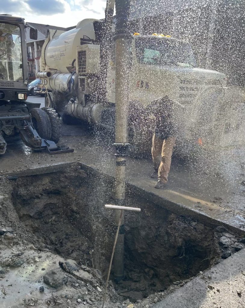 A man is pouring water into a hole in the street.